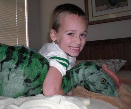 A boy is laying on the bed with his stuffed animal.