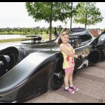 A little girl standing next to a batmobile