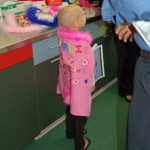 A child in a pink coat standing next to a counter.