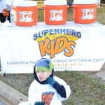 A young boy in a superhero costume stands next to some buckets.
