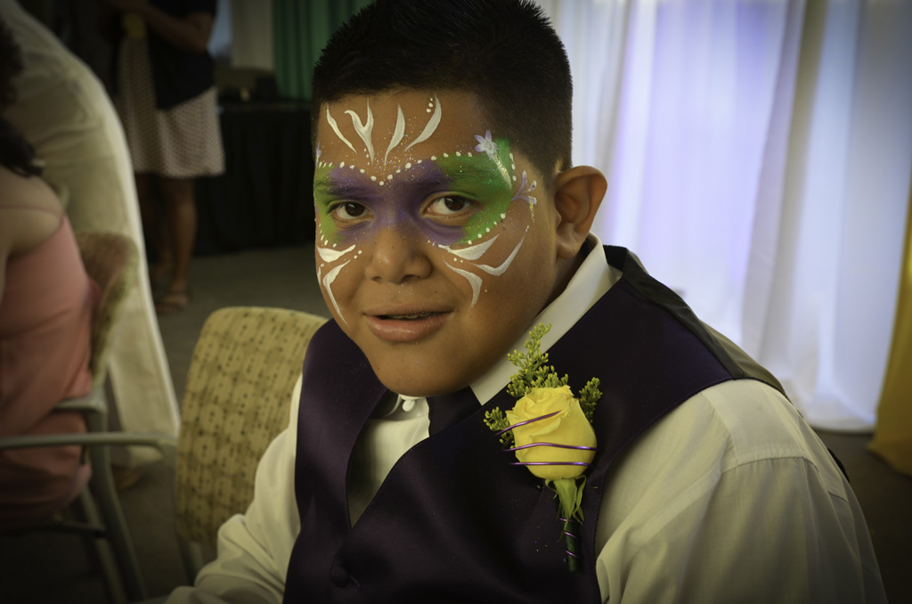 A boy with face paint and a flower in his hair.