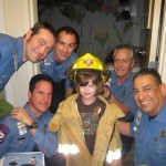 A group of men standing around a girl in a fireman 's outfit.