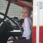 A young girl sitting in the driver 's seat of a fire truck.