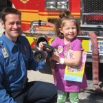 A little girl is holding her camera and posing with a fireman.