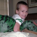 A boy is smiling while holding two stuffed animals.