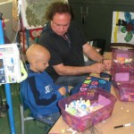 A man and boy sitting at table with boxes of art supplies.