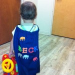 A little boy in a blue cape holding a toy.