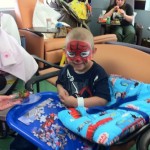 A young boy with spiderman face paint sitting in a chair.