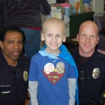 A boy with leukemia is surrounded by two police officers.