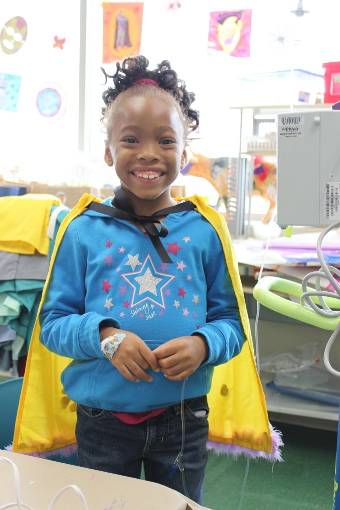 A young girl wearing a blue star shirt and yellow cape.