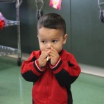 A little boy in red jacket holding his hands to his mouth.