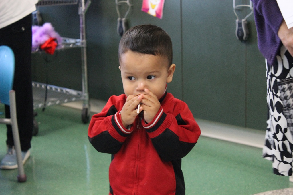 A little boy in red jacket holding his hands to his mouth.
