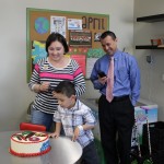 A boy is cutting his birthday cake with two adults.