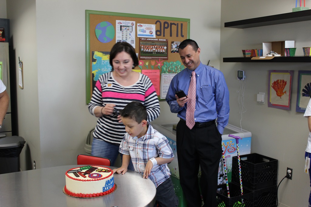 A boy is cutting his birthday cake with two adults.