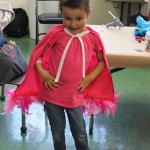 A little girl in a pink cape standing on the floor