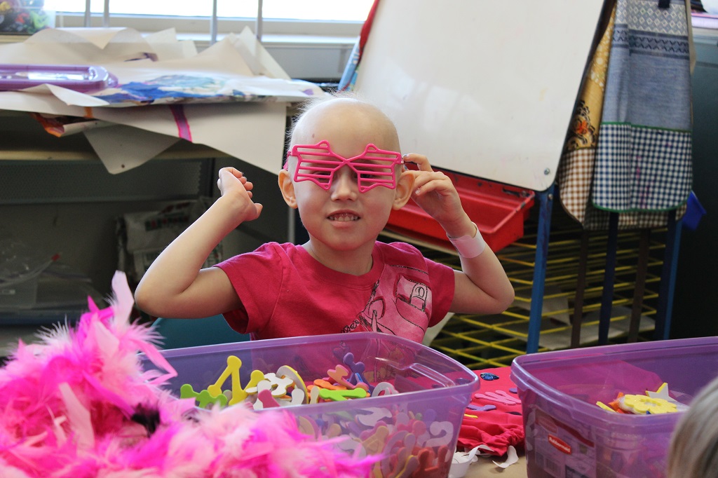 A young girl wearing pink glasses and holding onto her hair.
