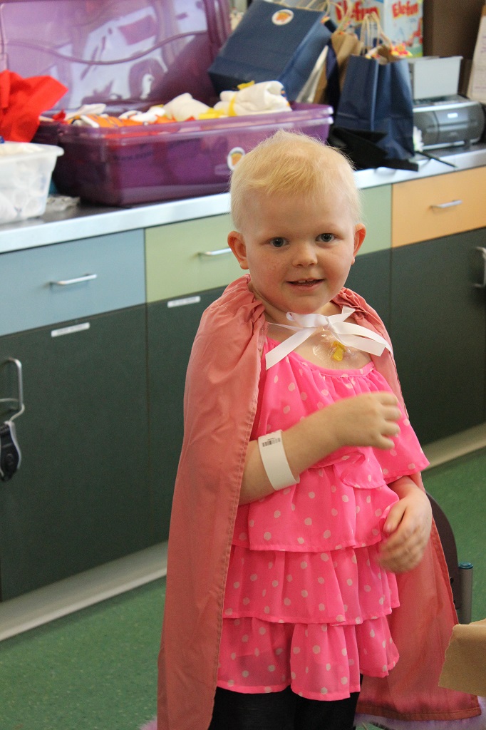 A little girl in pink dress and cape.
