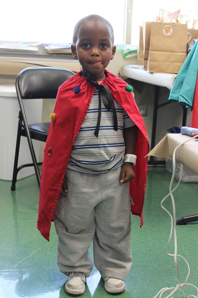 A young boy wearing a red cape and grey pants.