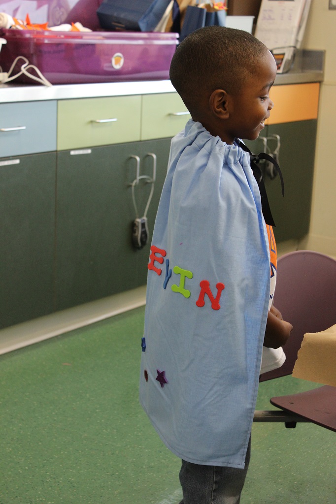 A young boy wearing a cape and holding a mirror.