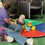 A woman and baby playing with toys on the floor.
