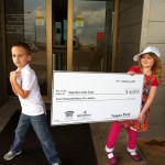 Two children holding a giant check in front of a building.