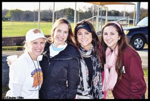 Four women are posing for a picture at the baseball game.