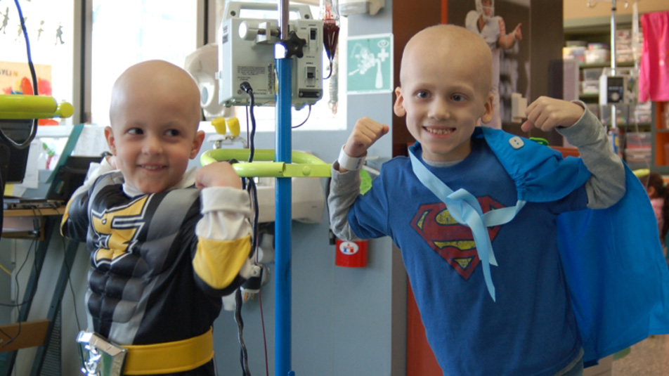 Two boys with shaved heads and one is wearing a batman costume.