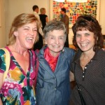 Three women smile for a picture in front of a painting.