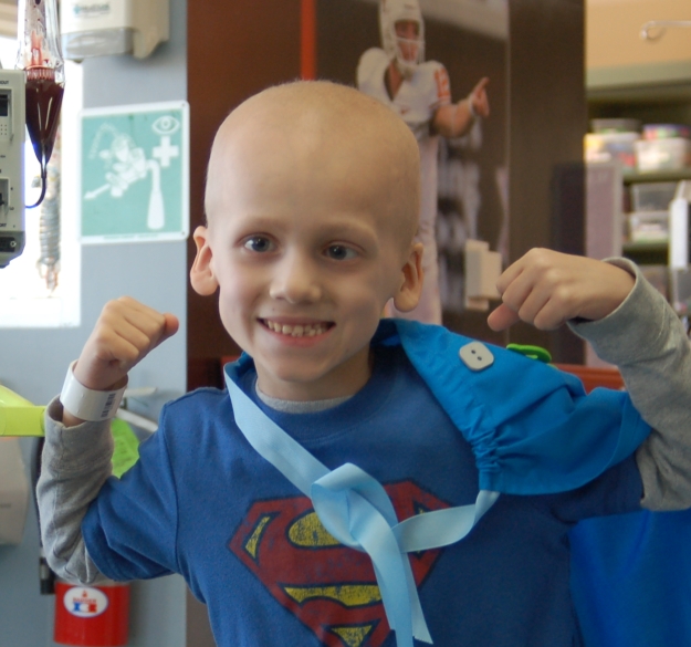 A young boy with a blue shirt and superman logo on his head.